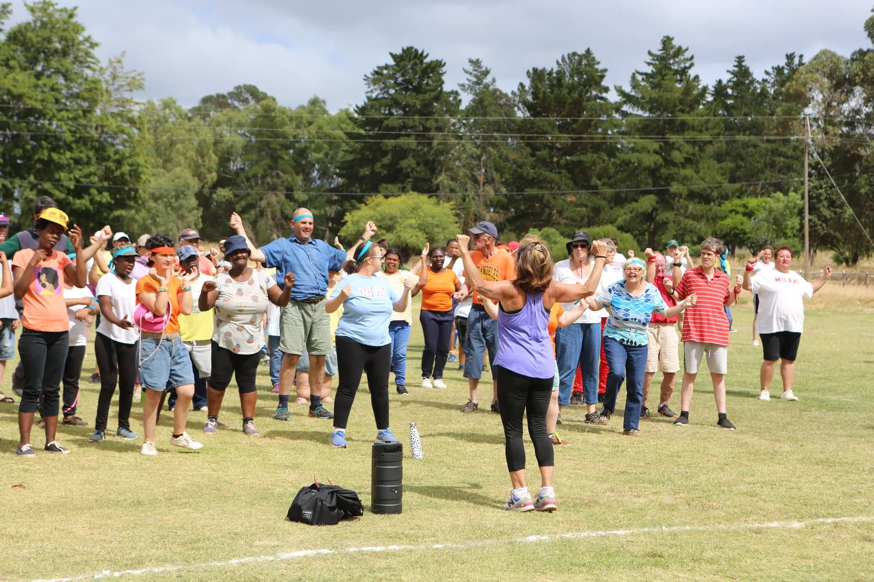 Residents and staff spread across the village sports field, arms raised, following a warm-up led by a staff member in front of the group.