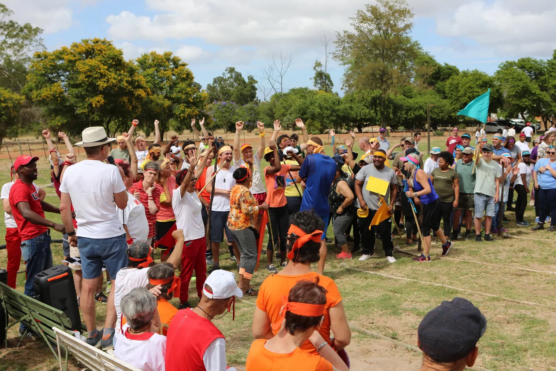 Residents, co-workers and volunteers packed together on the sports field at Camphill Village, cheering with their arms raised as a teal flag flies behind them